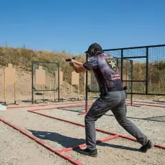 Strzelec w dynamicznej postawie podczas zawodów IPSC. To właśnie ipsc co to jest? To strzelectwo dynamiczne, gdzie liczy się szybkość i celność.