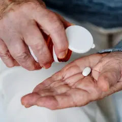 Manos de anciano vertiendo una pastilla blanca en su palma para tomar magnesio.