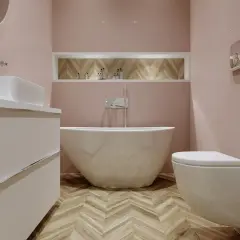 Elegancka łazienka z wolnostojącą wanną i baterią wannową. Jasnoróżowe ściany, drewniana podłoga w jodełkę.