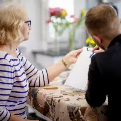 Starsza pani z niebieskimi okularami i młody mężczyzna omawiają wniosek o rejestrację pojazdu przykład.