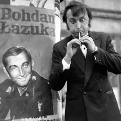 Bohdan Łazuka w garniturze, z papierosem w ustach, obok plakatu z jego podobizną.