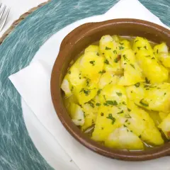Delicioso bacalao a la cazuela, con trozos tiernos de pescado en una salsa dorada y perejil picado, servido en una cazuela de barro.