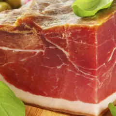 Ein Block Parma-Schinken, mariniert mit Kräutern, daneben grüne Oliven. Was ist Parmaschinken? Ein Genuss!