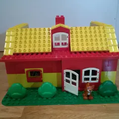 Ein farbenfrohes Lego Duplo Haus mit gelbem Dach, roten Wänden, Fenstern, einer Tür und einem kleinen Fuchs davor. Perfekt für kreative Bauanleitungen.