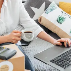 Kobieta z kawą uczy się, jak sprzedawać na OLX, korzystając z laptopa i kalkulatora.