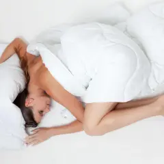 En andfådd gravid kvinna sover på sidan, insvept i ett vitt täcke.