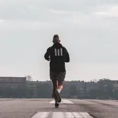 Mężczyzna w czarnej bluzie z trzema paskami biegnie po asfalcie. To jego trening bieganie w terenie.