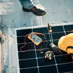 Instalatorzy sprawdzają panel słoneczny. Na panelu leżą miernik, żółty kask, krótkofalówka i taśma miernicza. Zabezpieczenie przeciwprzepięciowe jest kluczowe.