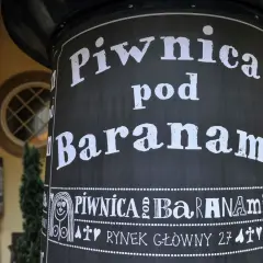 Czarny słup z białym napisem "Piwnica pod Baranami" i ozdobnymi elementami.