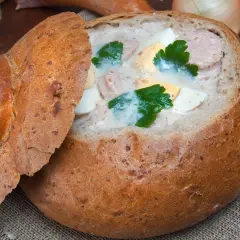 Pyszny żurek w chlebie, z kiełbasą i jajkiem, ozdobiony natką pietruszki. Idealny na polski obiad.