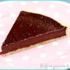 Une part de tarte au chocolat facile, avec une garniture riche et une pâte croustillante, servie sur une assiette rose à pois blancs.