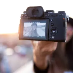 Aparat fotograficzny trzymany przez rękę, na ekranie selfie uśmiechniętej kobiety.