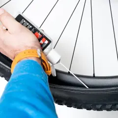 Ręka wylewa płyn do opony bezdętkowej roweru, przygotowując ją do jazdy.