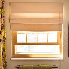 A beige Roman shade is partially lowered over a window, showing how to make Roman shades with its neat folds.