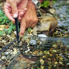 Main tenant fixe un filet sur des galets près de l'eau. Ce filet protège les poissons, ce que mange un héron, des prédateurs.