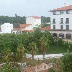 Edificio blanco con tejado naranja, palmeras y vegetación exuberante. Parece el hotel El Paso PortAventura, listo para recibir a sus huéspedes.