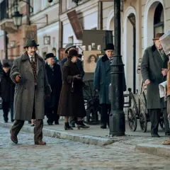 Ulica w stylu retro, gdzie kręcono film Znachor. Ludzie w płaszczach i kapeluszach spacerują po bruku.