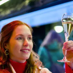 Frau mit roten Haaren hebt ein Glas Sekt, das auf der Hefe gereift ist, in festlicher Beleuchtung.