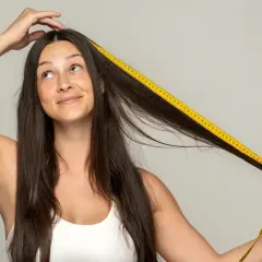 Mujer se mide el pelo con cinta métrica amarilla, preguntándose cuánto tarda el pelo en crecer.