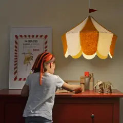 Una niña juega con bloques de madera bajo una lámpara colgante infantil con forma de carpa de circo.