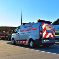 Pojazd ponadgabarytowy transportowany na platformie, eskortowany przez dwa samochody pilotujące z napisem "PILOT".