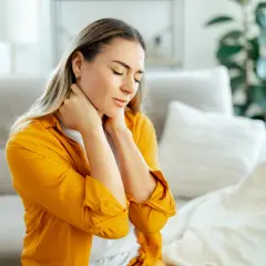 Donna con occhi chiusi e mani sul collo, soffre di dolori muscolari diffusi.