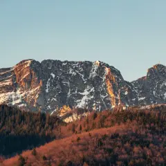 Giewont w słońcu, z ośnieżonymi zboczami i lasem u podnóża. Jego imponująca wysokość robi wrażenie.