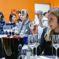 Dégustation de vin à Wine Paris 2026. Une femme hume un verre, casque sur les oreilles, entourée d'autres participants.