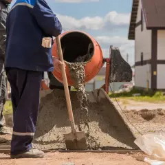 Dwóch budowlańców pracuje przy betoniarce. Wylewa się z niej świeży beton. Pytanie: ile cementu na betoniarkę 200?