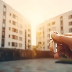 Dłoń trzymająca klucz przed budynkiem mieszkalnym.