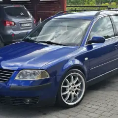 Błękitny Passat B5 1.9 TDI 130KM na aluminiowych felgach, zaparkowany na podjeździe obok szarego SUV-a.