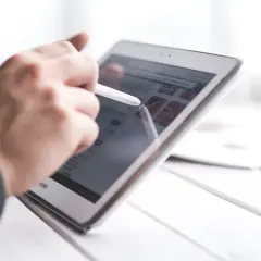 Ręka z rysikiem na tablecie, przeglądająca stronę internetową. Dowiedz się, jak zablokować życzenia na FB.