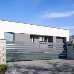 Nowoczesna, szara brama przesuwna z poziomymi listwami, prowadząca do minimalistycznego domu z białym tynkiem.