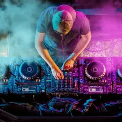 DJ con mani sui piatti, luci al neon e fumo creano l'atmosfera perfetta per la musica house famosa.