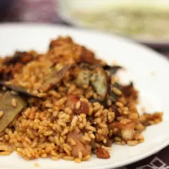 Deliciosa paella de conejo con trozos de carne dorada y verduras, servida en un plato blanco.