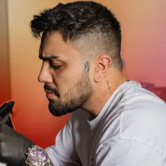 Un homme se fait tatouer le cou, un tatouage homme cou discret avec des motifs rouges. Il porte des gants noirs et une montre.