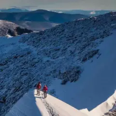 Två vandrare på en snöig bergskam med Kebnekaise i bakgrunden. En bra kebnekaise packlista är avgörande för en säker tur.
