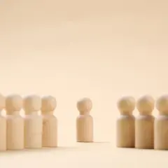 Un pupazzetto di legno si erge da solo, separato da un gruppo. Un simbolo di imparare a stare da soli, trovando forza nella propria individualità.