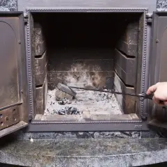 Maintenant, que faire de la suie de cheminée ? Une main utilise une pince pour nettoyer les cendres et la suie d'un foyer ouvert.