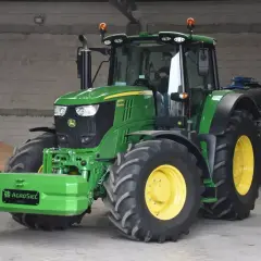Zielony John Deere 6195M, z kierowcą w kabinie, stoi obok przyczepy. Czy to najlepsza marka ciągnika?