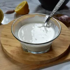 Kremowe aioli w miseczce, obok cytryna i czosnek. Idealne do dipów i sosów.