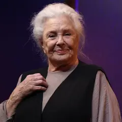 Lola Herrera, con su melena plateada y una sonrisa serena, luce un chaleco negro sobre una blusa beige. Su mano izquierda, con un anillo, reposa sobre su pecho.