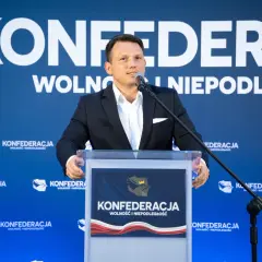 Mężczyzna w garniturze przemawia na tle logo Konfederacji. Czy to zapowiedź sekretów negocjacji Konfederacji z rolnikami w sprawie blokad granic w marcu 2026?