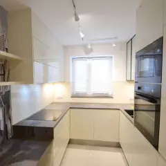Nowoczesna kuchnia z oknem na środku, z fototapetą przedstawiającą uliczkę. Jasne szafki i ciemny blat tworzą elegancką całość.