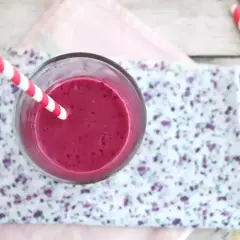 En glas med en lila indisk yoghurtdryck, med ett rött och vitt randigt sugrör.
