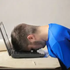 Frustrierter Mann mit Kopf auf Laptop. Er sucht nach einem Musterbrief für den Widerruf einer Abo-Falle.