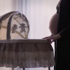 Gravid kvinna med händerna på en vagga med nallar, en fixerad bebis väntar.