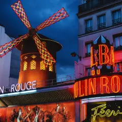 Le Moulin Rouge à Paris s'illumine la nuit, ses ailes de moulin rouge et jaune dansant sous le ciel sombre.