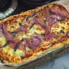 Frisch gebackene Pinsa mit zartem Schinken und geschmolzenem Käse auf rustikalem Holzbrett. Ein Genuss für jeden, der gerne Pinsa backen möchte.