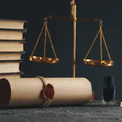 Waga sprawiedliwości, księgi i pieczęć na zwoju. Kto opłaca notariusza przy sprzedaży mieszkania? Zazwyczaj kupujący.